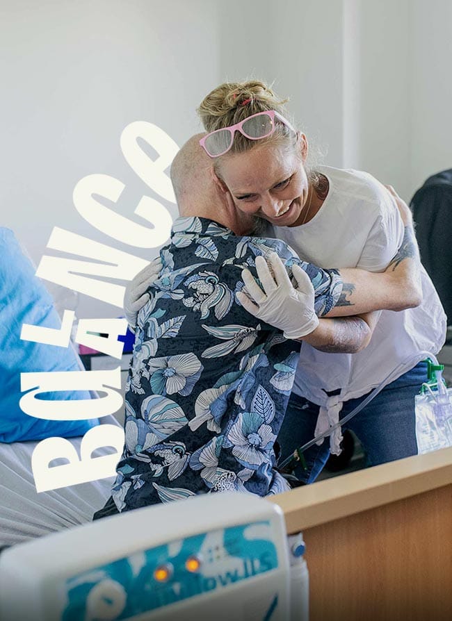 Two people hugging in a hospital room with the word Balance as lettering