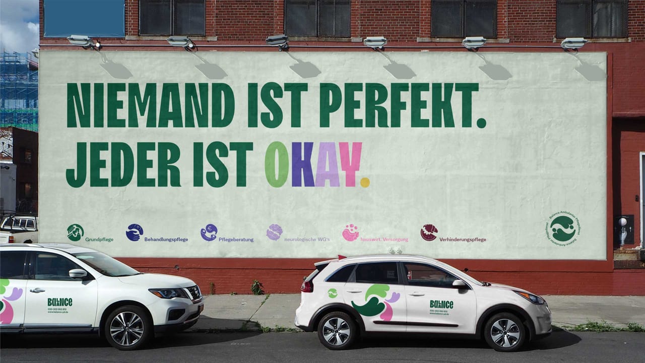 Billboard “Niemand ist perfekt. Jeder ist okay.” with the service icons, and two white Balance cars with colorful livery