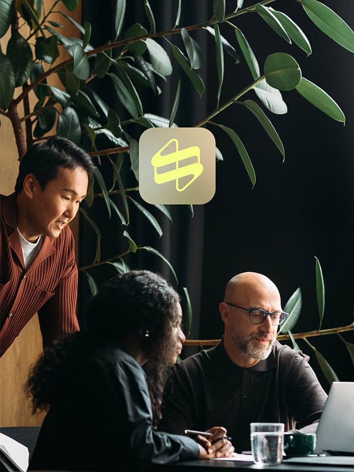 People work on laptops in an office with plants in the background