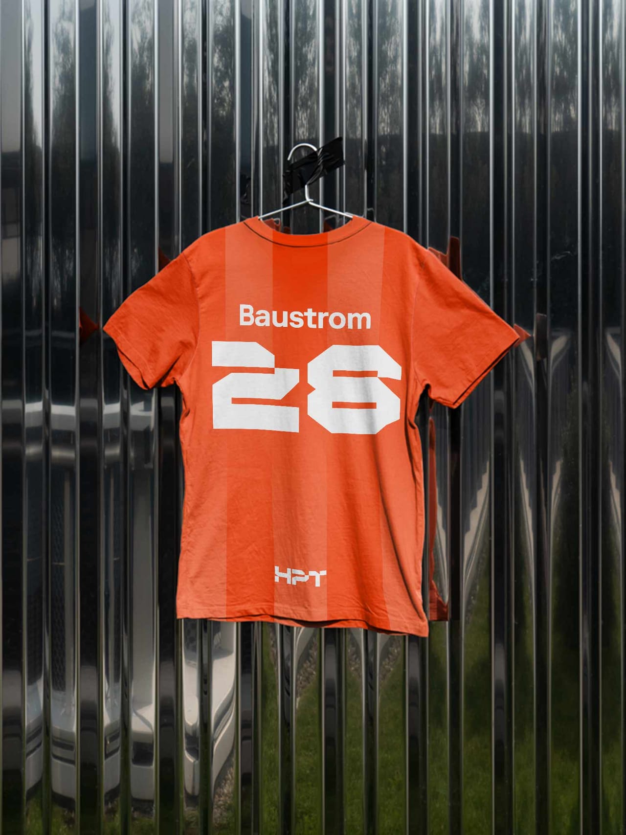 Orange HPT work shirt “Baustrom 28” hanging in front of a corrugated metal wall