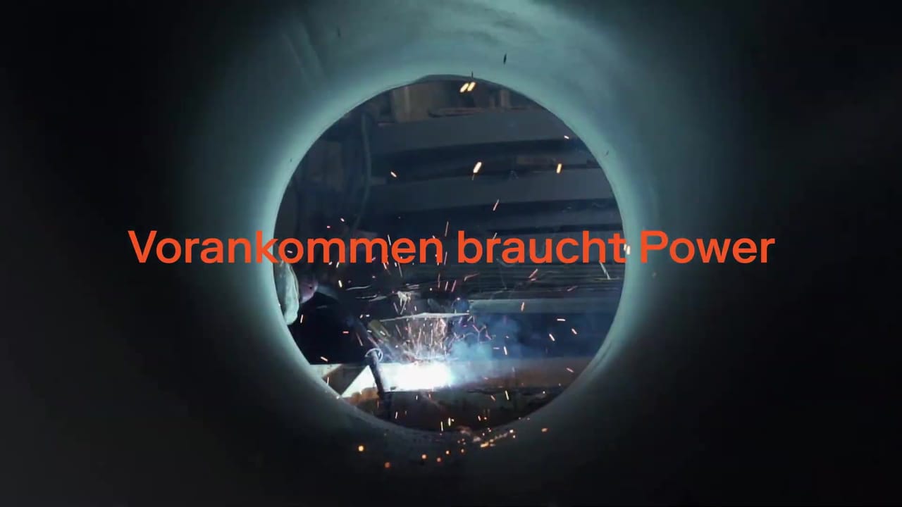 Welding sparks seen through a pipe with the orange headline “Vorankommen braucht Power”