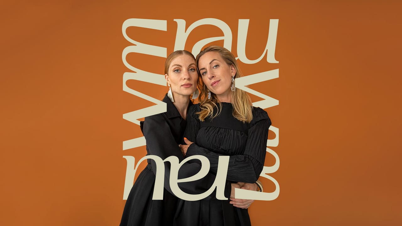 Two women in black dresses embrace in front of an orange backdrop; the letters of the rauwm wordmark wind around them in beige
