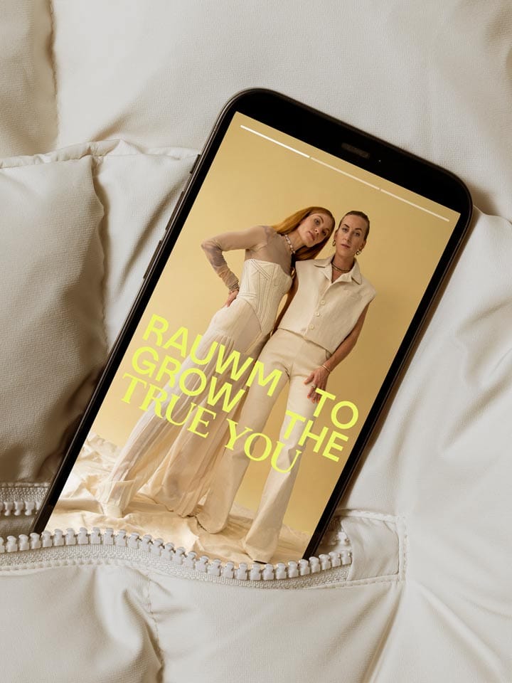 A phone in a cream down jacket pocket shows a story of the two founders in cream, with the claim in yellow