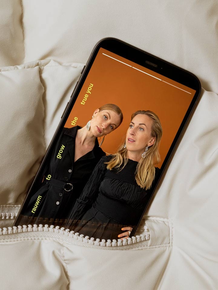 A phone in a cream down jacket pocket shows a story of the two founders in black on orange
