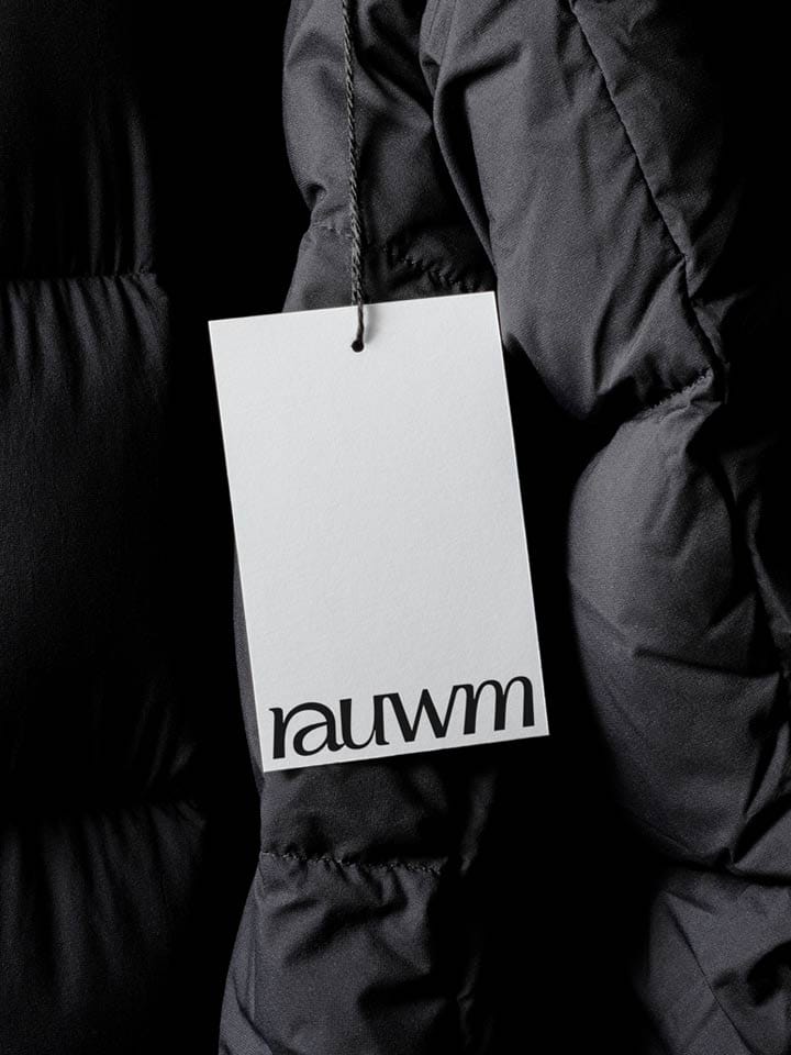 A white clothing tag with the rauwm wordmark hangs on a black down jacket