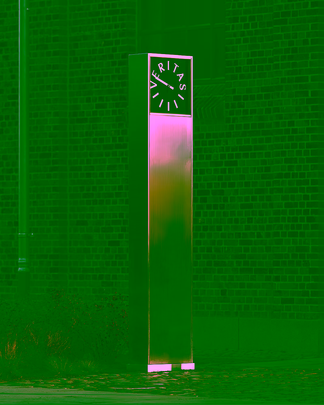 Metal VERITAS clock pillar in front of a brick wall