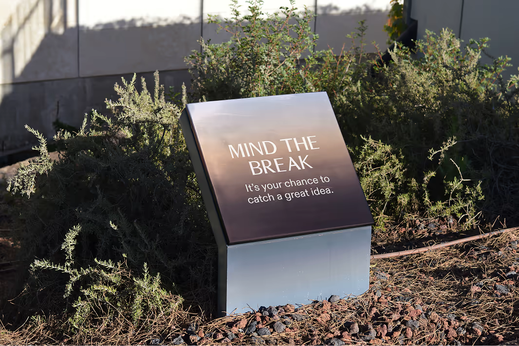 A metal VERITAS sign “Mind the break” in a garden